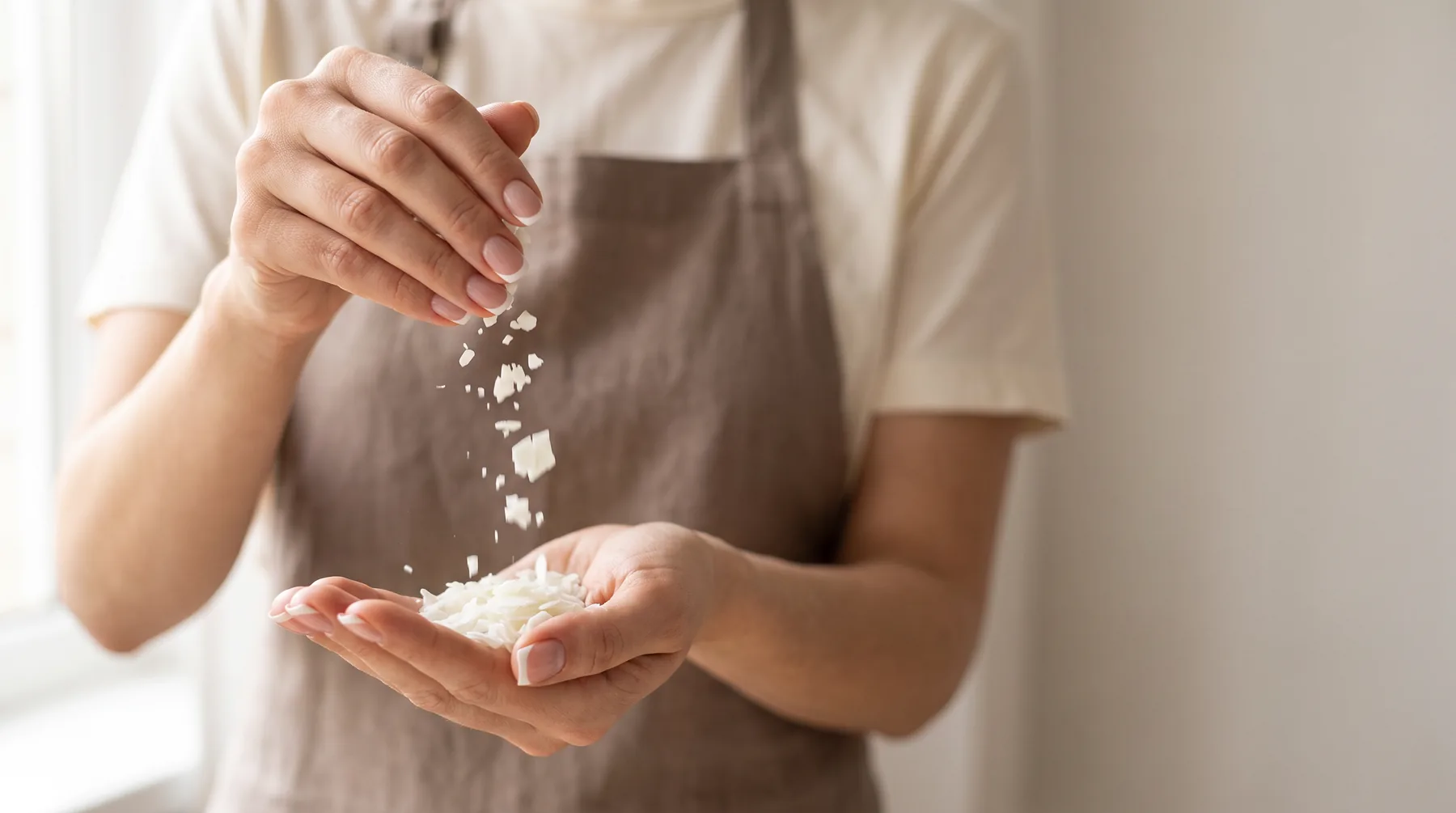 Wax flakes falling into cupped hands in soft window light